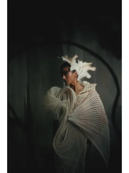 An ethereal shot where the model and the sculptural white dress appear to be emerging from the shadows. The styling and lighting work together to create a ghostly, high-fashion image.