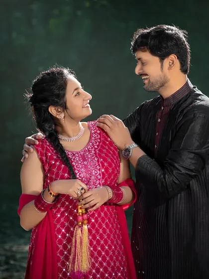 A sweet, loving glance shared between the couple, dressed in colorful ethnic wear. The natural, green background provides a simple yet beautiful setting for this portrait.
