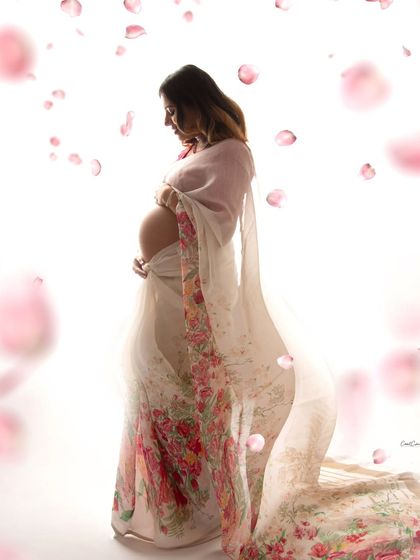 A dreamy and artistic silhouette of a mom-to-be in a floral saree, surrounded by a shower of soft pink petals.