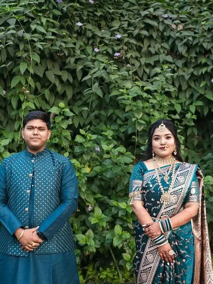 A classic, beautifully balanced couple portrait. The symmetrical composition against the wall of green foliage allows the couple's elegant traditional attire and calm expressions to be the central focus of the image.