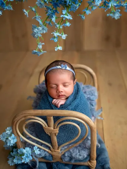 A tiny bed prop creates such an adorable scene. Here, a swaddled newborn sleeps peacefully under delicate blue flowers, a setup we practice during the workshop to master prop-based posing.