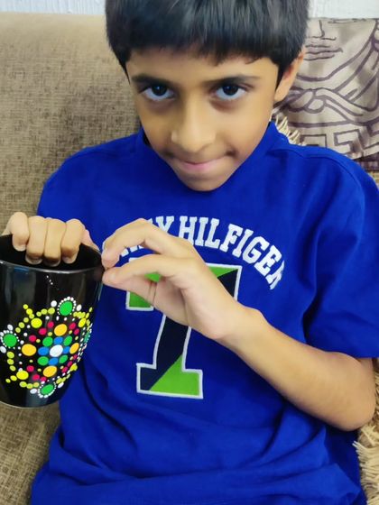 A young boy proudly displays the colorful dot mandala pattern he created on his mug at the party.
