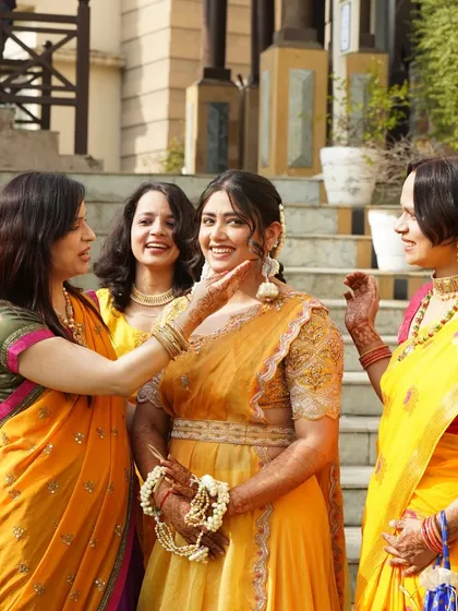 The bride is surrounded by her family, who lovingly apply Haldi to her face.