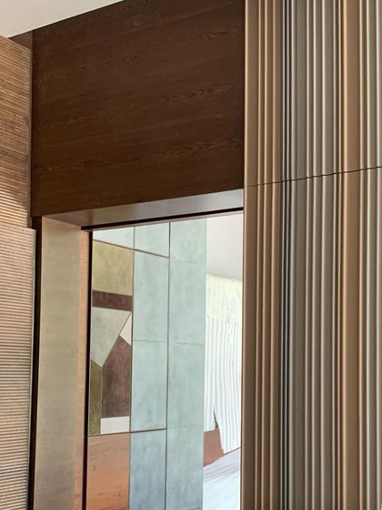 A glimpse through a doorway, revealing layers of texture. Fluted wall panels, wood grain, and a geometric leather-clad wall in the distance create a rich and complex interior composition.