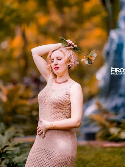 An artistic solo portrait of a model in a garden setting, with a flower adding a delicate touch.