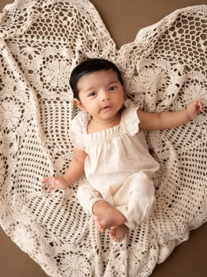 A simple and sweet portrait of a baby girl lying on a heart-shaped crochet blanket. Her direct gaze and cute outfit make this a lovely milestone photo.