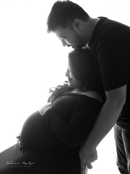 A tender moment captured in silhouette. The dad-to-be kisses his partner's forehead, a gesture of love and support that is beautifully conveyed through their shadows.