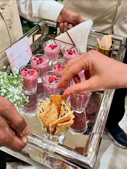 A server offering guests shots of our colourful beetroot hummus with lavash crackers on a silver tray.