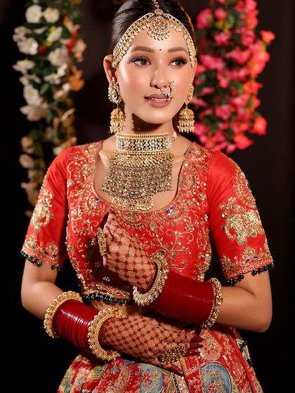 This bride looks radiant and happy. The makeup is fresh and glowing, with a focus on enhancing her natural features to match her beautiful red and gold outfit.
