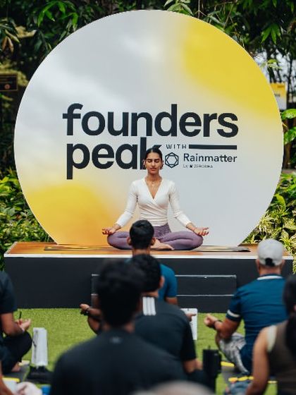 A yoga instructor leads a session for founders at the Rainmatter retreat, set against a custom event backdrop.