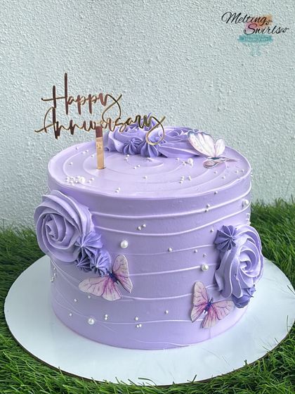An elegant purple anniversary cake decorated with piped rosettes and delicate wafer paper butterflies. The silver "Happy Anniversary" topper completes the look.