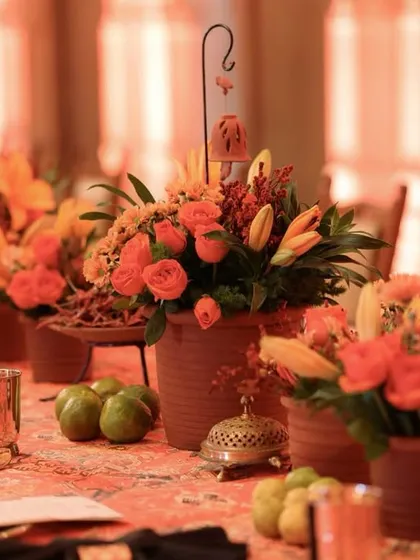 A table runner of terracotta pots filled with orange roses and lilies, interspersed with fresh green apples and traditional brass incense burners.