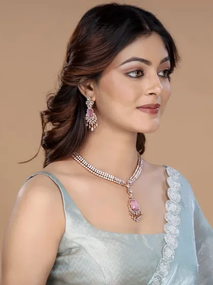 A model displays a modern necklace set with a pink teardrop pendant. The three-quarter profile is a classic pose for catalogue photography, showing how the jewellery sits elegantly.