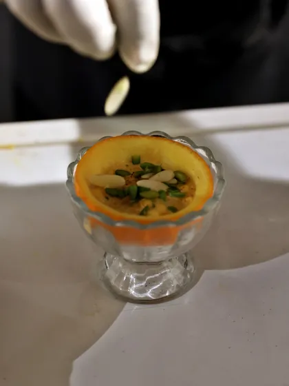 A traditional Indian dessert served in a hollowed-out orange peel, garnished with slivered almonds. A creative and beautiful presentation.