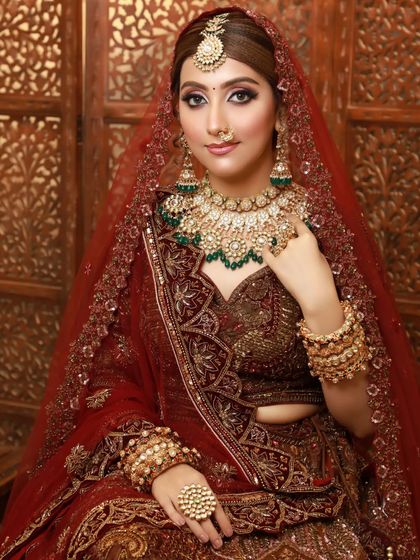 A full portrait of a bride in a deep red lehenga. The makeup is classic and regal, designed to make a statement.