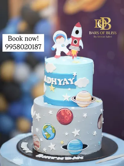 A two-tiered space exploration cake perfect for a young astronaut's birthday. The design features edible planets, stars, a rocket ship, and an astronaut, creating an out-of-this-world celebration centerpiece.