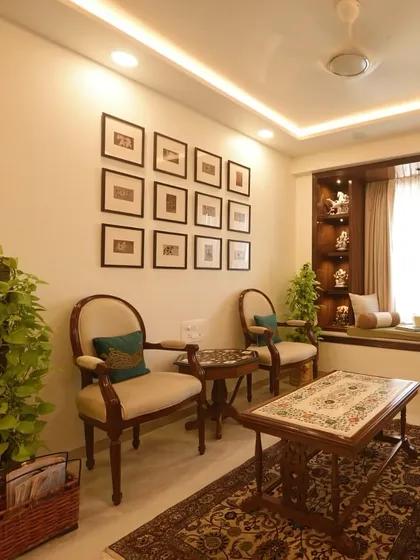 A closer look at the seating area, showcasing the elegant armchairs and the gallery wall of framed prints. The addition of indoor plants brings a touch of nature and life into the space.