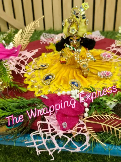 A beautifully decorated Kanha ji idol, dressed in a yellow poshak, as part of a Teej festival gift set.