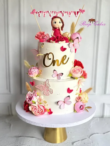 A special cake for a special day. This two-tier first birthday cake is filled with flowers, butterflies, and a custom fondant doll.