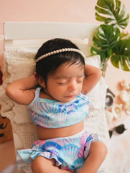 A close-up of the little beach bum, sleeping peacefully. The details like the monstera leaf and toy plane add to the vacation vibe.