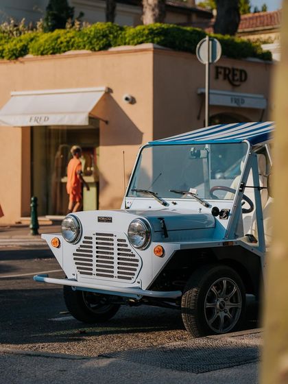 A vintage Mini Moke car, a classic sight in St. Tropez, parked on a sunny street. This captures the fun and stylish vibe of the French Riviera.