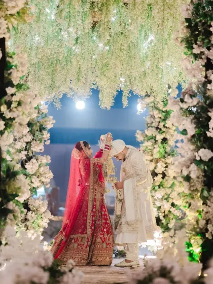 The varmala exchange, a playful and significant ritual, captured under a beautiful floral arch.
