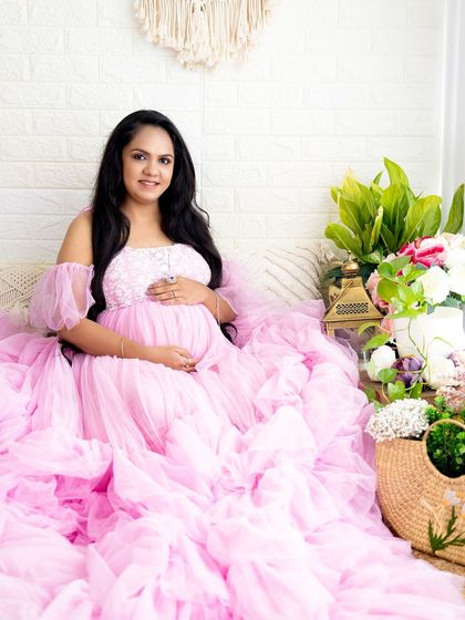 A vibrant portrait of a mom-to-be seated amongst lush greenery and flowers, her pink gown spreading out beautifully.