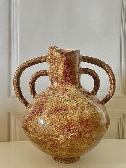This large, hand-built vase with four handles has a rustic, ancient feel. The warm, earthy glaze enhances its timeless quality, making it a substantial piece for any room.