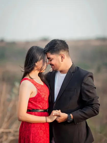 An intimate pre-wedding portrait of a couple holding hands, with their foreheads touching, set against a beautiful landscape.