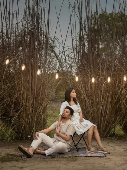 A beautifully lit outdoor evening shot. The string lights create a warm, magical glow around the couple, perfect for a romantic and whimsical pre-wedding theme.