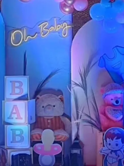 A close-up of a baby shower decoration with blue lighting, "BABY" blocks, and a teddy bear prop, creating a cozy and cute atmosphere.