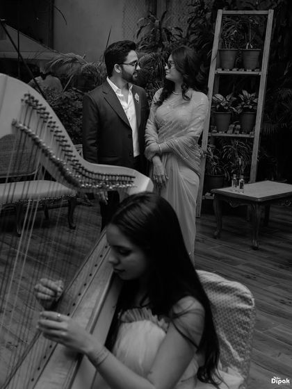 An artistic black and white photo of a couple enjoying a private moment with a harpist. This unique, atmospheric shot adds a layer of sophistication to your pre-wedding story.