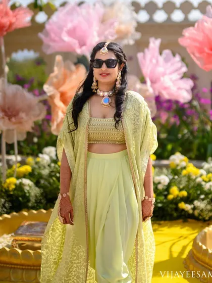 For pre-wedding festivities like Mehendi or Haldi, I create modern fusion wear. This ensemble features a lime green crop top with draped pants and a matching embroidered cape for a stylish and comfortable look.
