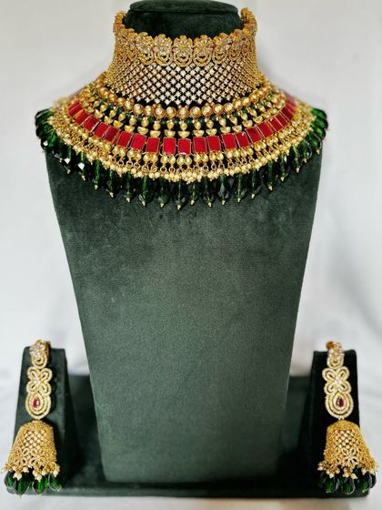 A colourful choker with red and green stones and a gold-plated finish. This rental set comes with matching jhumkas.