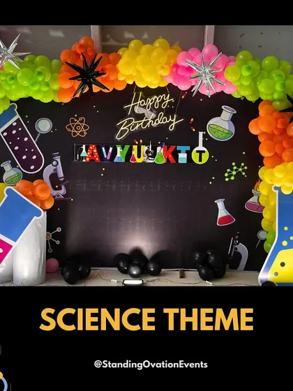 The main stage for the science themed party, featuring a chalkboard style backdrop, neon birthday sign, and cutouts of beakers and flasks, all framed by a vibrant balloon arch.