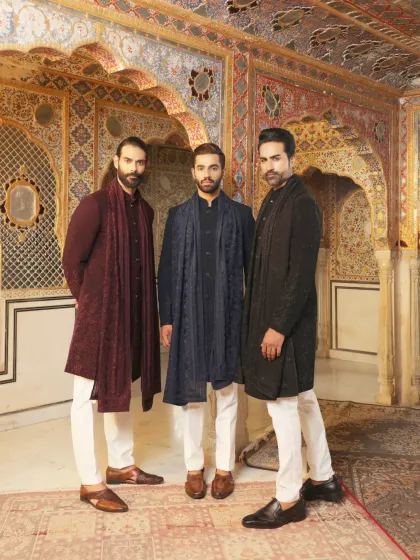 Dress your entire crew in our signature styles. This photo features three models showcasing a range of our festive wear, from a deep maroon sherwani with a matching stole to a navy blue piece with intricate embroidery, all designed to complement each other.