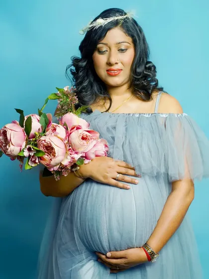 A simple and beautiful maternity portrait against a solid blue background, with the mom-to-be holding a bouquet of pink peonies.