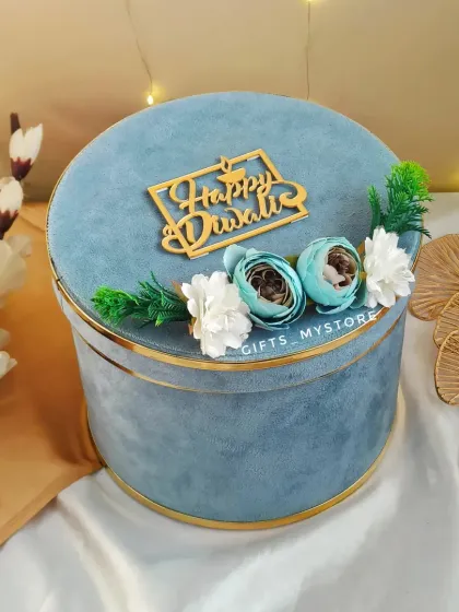 The closed view of our round velvet hamper box. The soft texture, gold trim, and floral accents make it a truly luxurious gift.