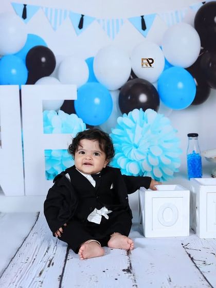 A baby boy in a black suit sits next to "ONE" blocks in the Boss Baby setup. This theme is a fun and creative way to celebrate a first birthday with style.