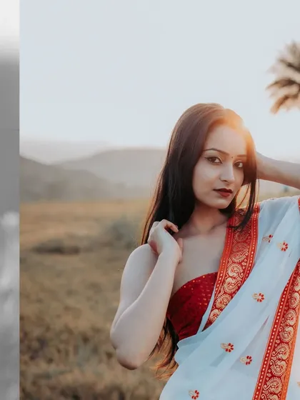 A golden hour portrait of a woman in a white and red Bengali saree, her face beautifully lit by the setting sun.
