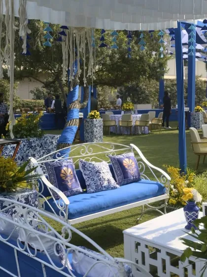 A cozy seating area with a white wrought-iron bench and blue cushions. The decor features a mix of traditional prints and modern elements, creating a unique and inviting space.
