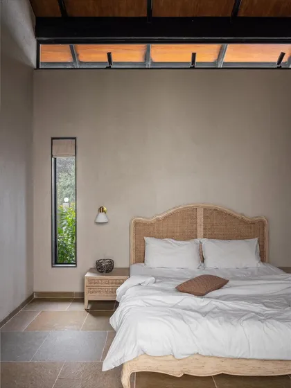 This bedroom in Grove House features a rattan headboard and is washed in natural light from the high clerestory windows. The simple, earthy materials and connection to the outdoors make it a perfect, restful space in this weekend home.