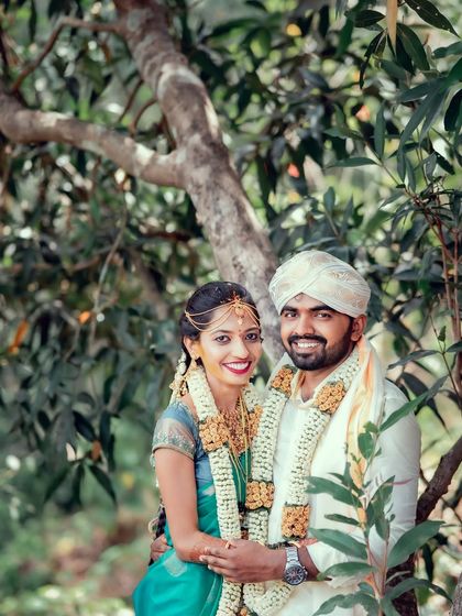 A happy South Indian couple posing for a portrait amidst lush green trees, their smiles radiating warmth.