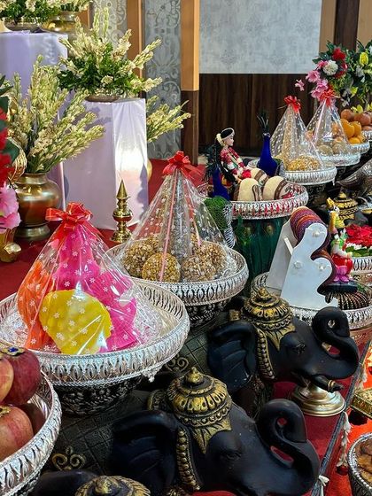 A variety of colorful sweets and offerings presented in silver bowls on black elephant stands.