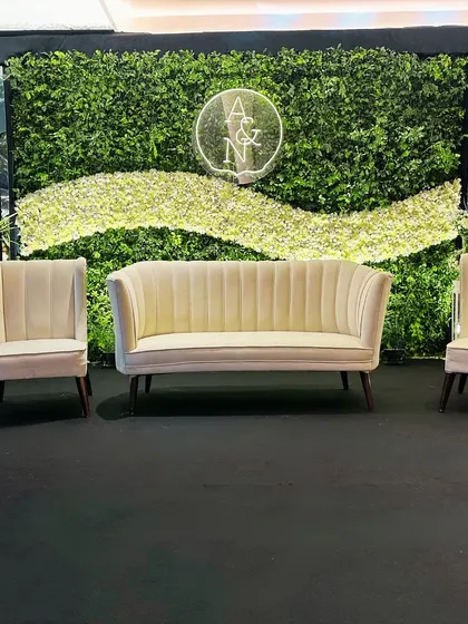 A clean, centered shot of the green and white reception stage, highlighting the modern furniture, neon monogram, and the elegant simplicity of the design.