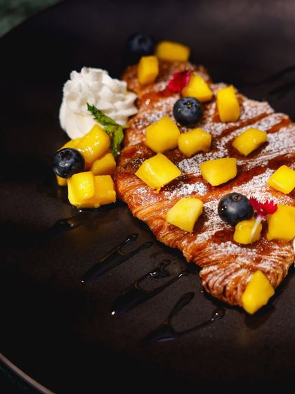 An artful close-up of our brunch croissant, showcasing the vibrant colors of the fresh fruit and a dusting of powdered sugar.