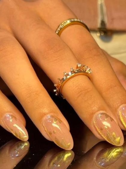 Another angle of the elegant gold foil nail art, styled with delicate gold rings.