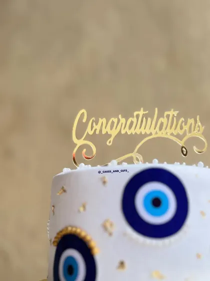 A detailed shot of the golden "Congratulations" topper on the evil eye cake.