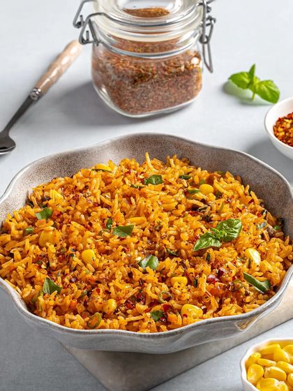 A bowl of spicy Schezwan fried rice, styled with fresh basil and chili flakes.