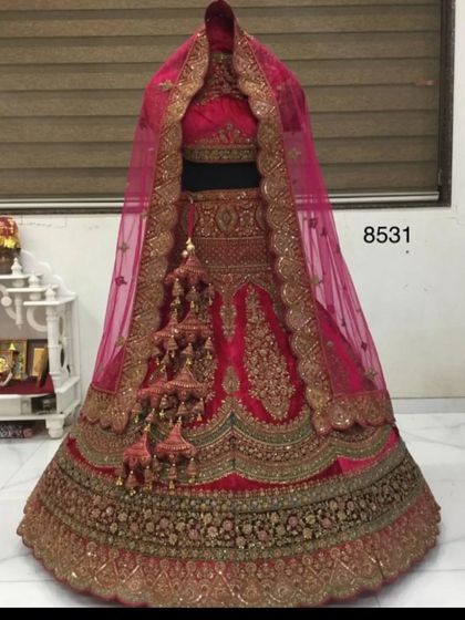 A mannequin display of a classic rani pink bridal lehenga. This piece features heavy gold zardozi work and traditional kalire, showcasing a quintessential North Indian bridal style.